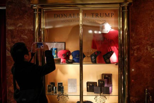 大厦里的玻璃柜内，展示着各种特朗普签名的周边产品，一男子站在柜前拍照。