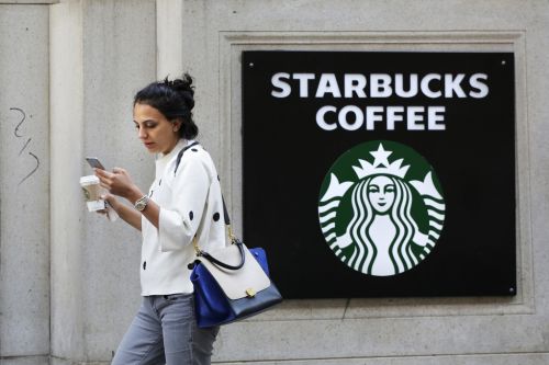 在纽约，一名女子手持星巴克咖啡杯，走过星巴克的标志（图片来源：美联社）